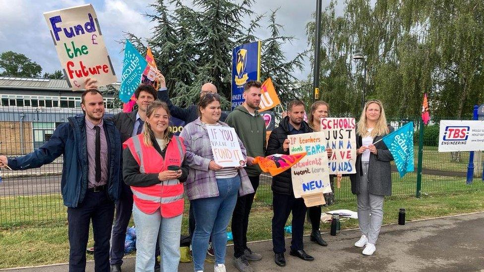 Nine people on a picket line holding placards