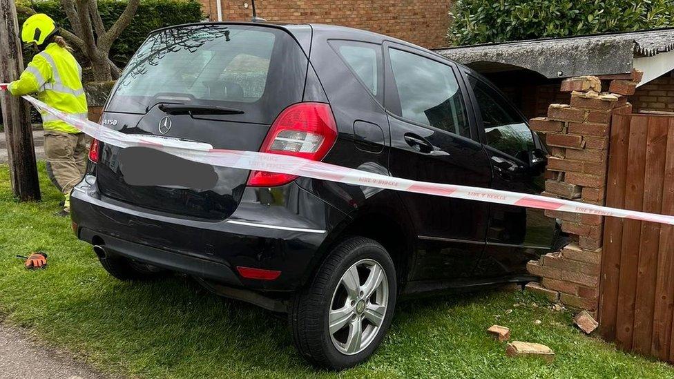 A Mercedes car that has crashed into a brick wall with a firefighter placing tape across it