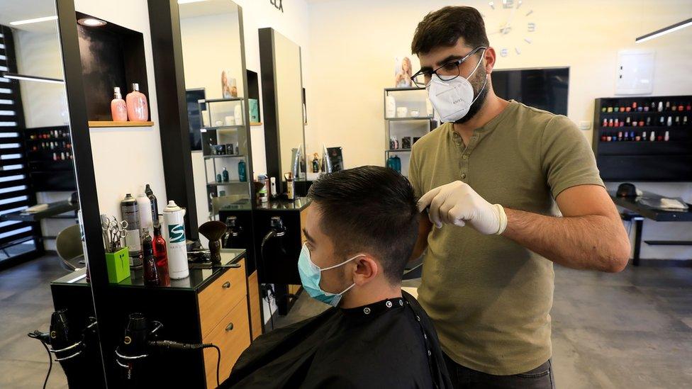 A man cuts hair while wearing medical gloves and a high-grade face mask in a hairdressers' shop