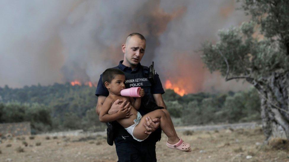 A Greek police officer carries a child away from wildfires