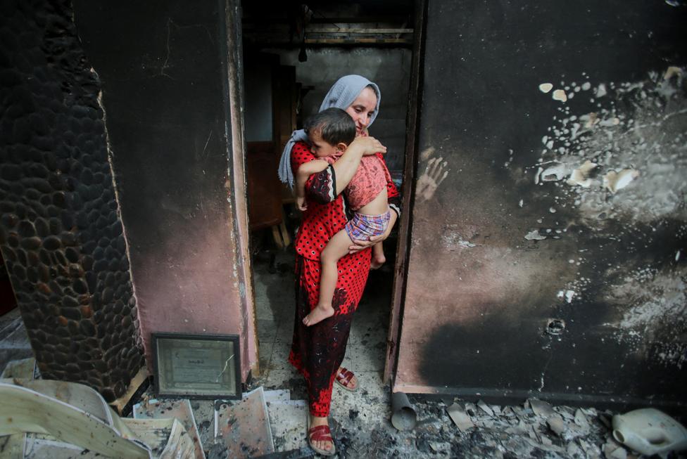 Souhila Belkati carries her child inside her burnt house, following a wildfire in Bejaia, Algeria July 25, 2023.