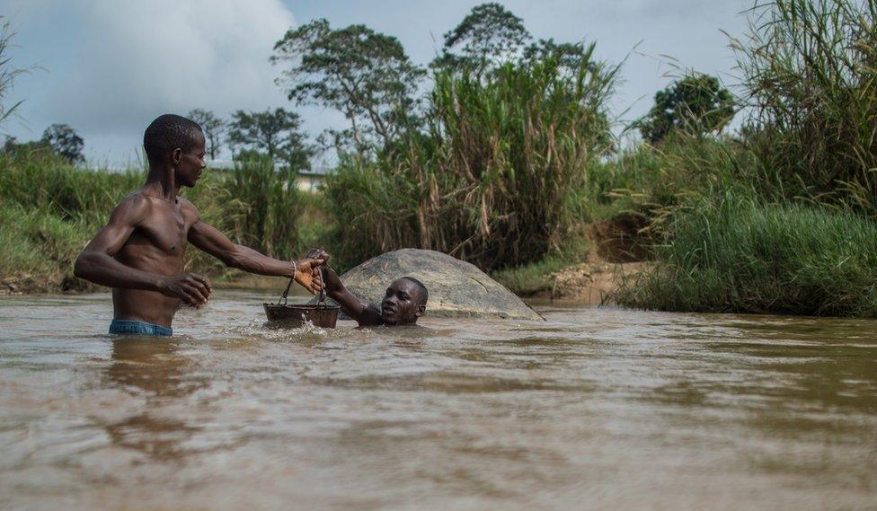 Men pass a bucket to each other whilst standing in the river