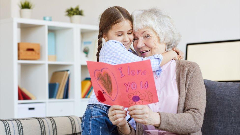 Grandmother hugging granddaughter and holding card.