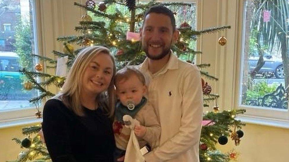 Adam and his wife Chrissy pose in front of a Christmas tree with their two children