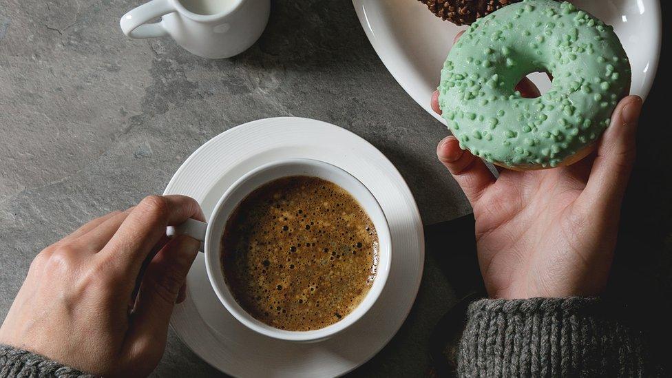 Plate of colorful glazed donuts with chopped chocolate, cup of black coffee