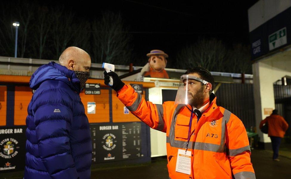 A Luton Town fan has their temperature taken whilst wearing a face mask