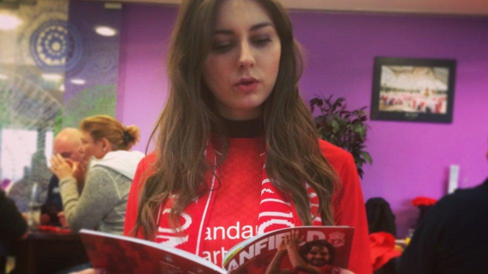 Hannah reading an Anfield brochure, wearing a Liverpool scarf