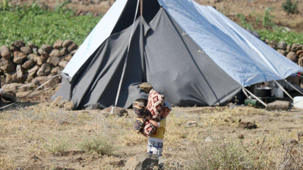 A displaced Syrian child carries cushions at a makeshift camp in the village of al-Rafid, near the Israeli-occupied Golan heights (27 June 2018)