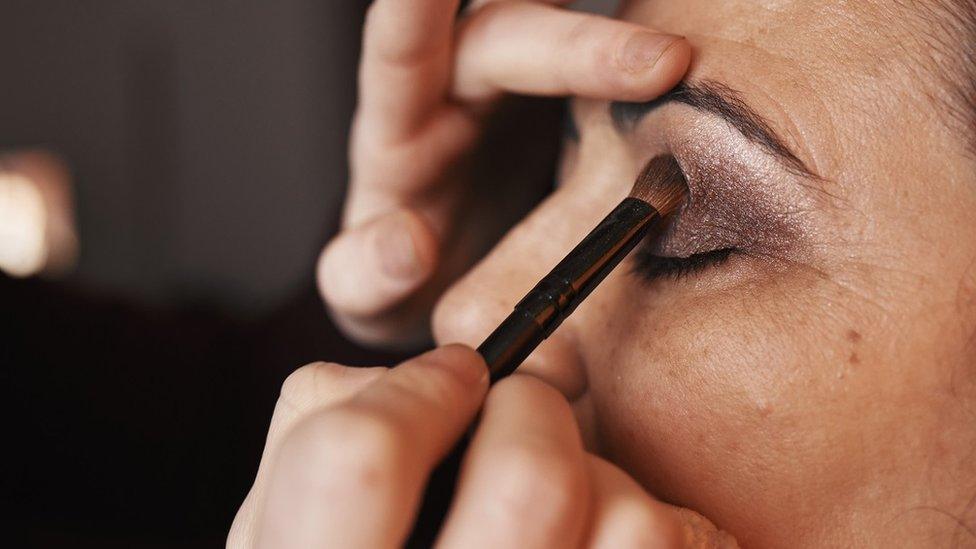 Eyeshadow is applied to a woman's left eyelid, side view