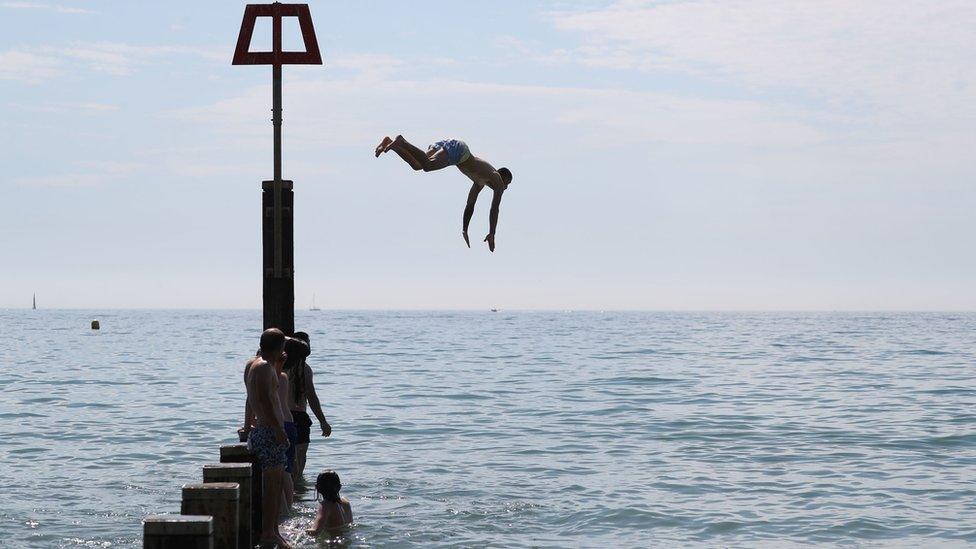 A man jumps off a groyne into the sea as they enjoy the hot weather at Bournemouth beach in Dorset