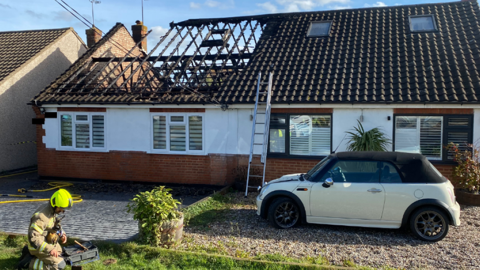 Bungalow with roof missing and charred timbers on display.