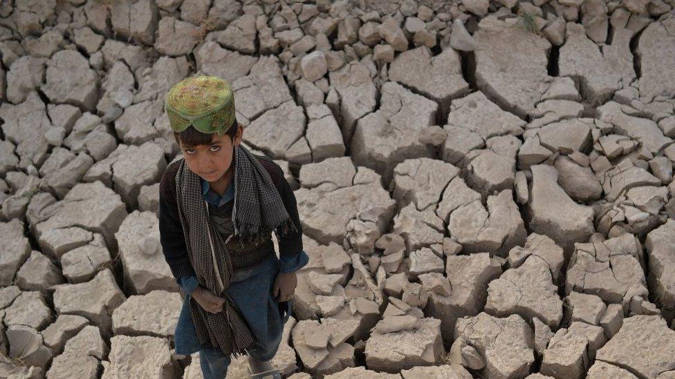 a boy walks along dry land with lots of cracks in the soil