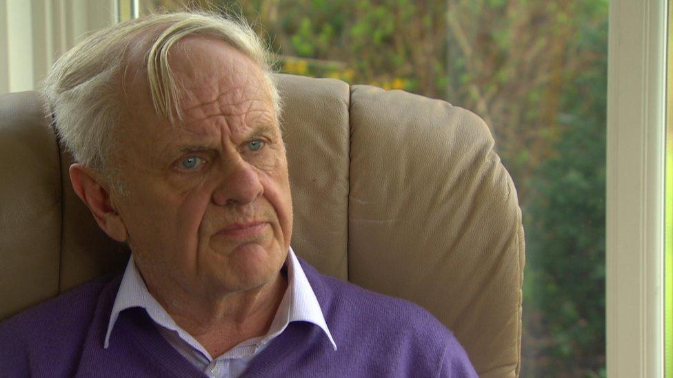 Reverend Norman Hamilton sits in a chair, wearing a purple jumper