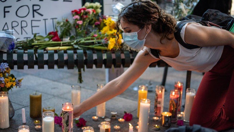 A person lays down a candle at a vigil for Garrett Foster the day after the shooting