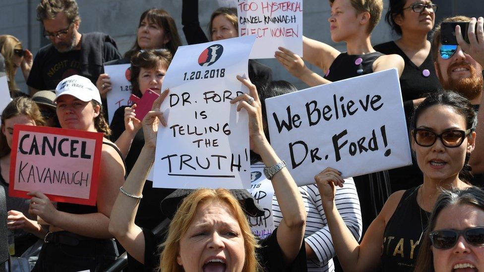 Demonstrators hold anti-Kavanaugh hold posters outside City Hall in Los Angeles on 28 September