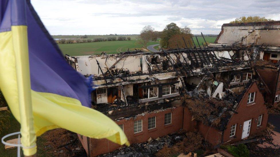 A Ukrainian flag flies from a building opposite a hotel used to house refugees from Ukraine that is now a charred ruin following what police suspect was an arson attack days before in the hamlet of Gross Stroemkendorf on October 24, 2022 n