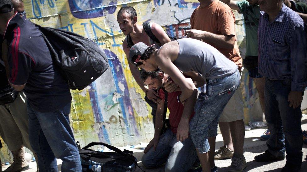 A man collapses as he waits to be registered by police outside a new registration centre at a stadium on the Greek island of Lesbos on 8 September 2015