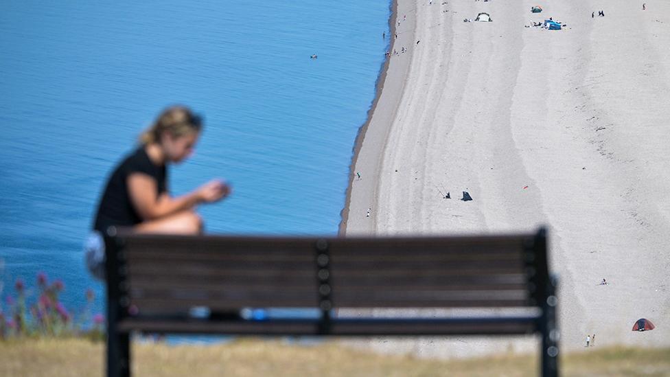 A person sits on the edge of a bench overlooking Chesil Beach, on July 10, 2022 in Portland, England.