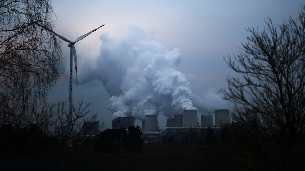 Water vapour rises from cooling towers beside a wind turbine in Jaenschwalde, Germany