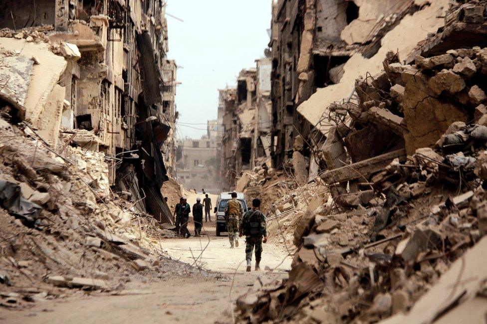 Soldiers walk past damaged buildings in the Yarmouk Palestinian refugee camp in Damascus (22 May 2018)