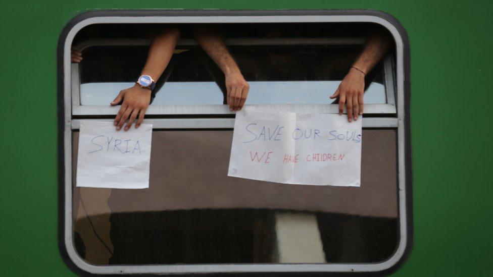 People on train at Budapest Railway Station hold signs saying "Save our souls"