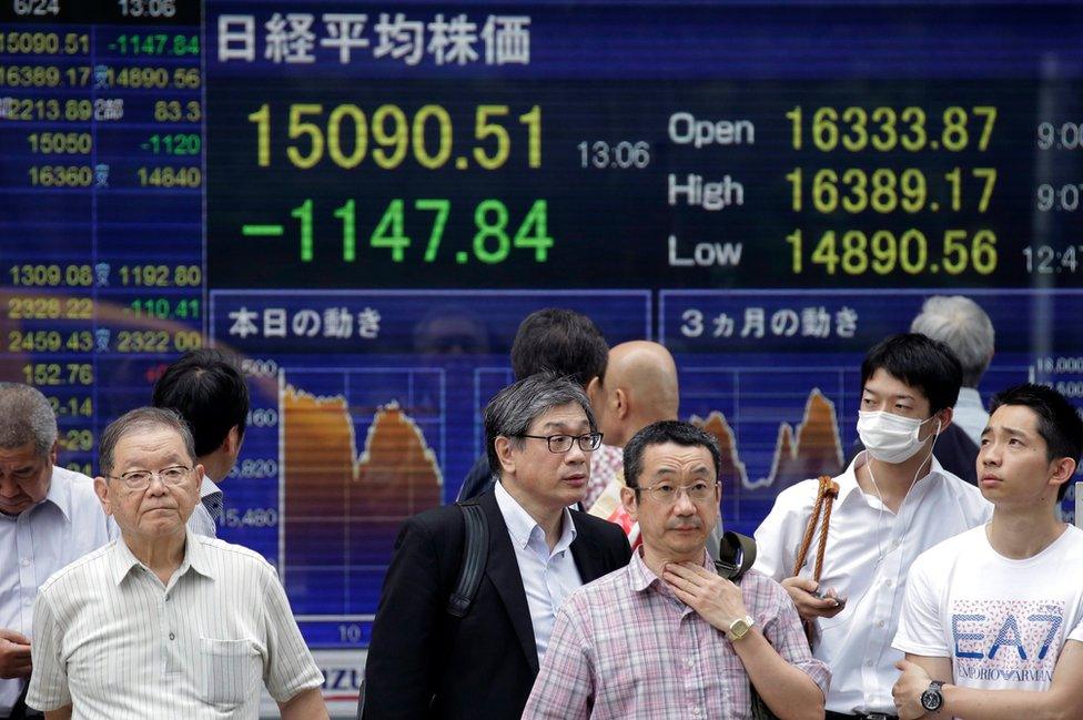 Pedestrians stand in front of a monitor displaying the Tokyo stock index