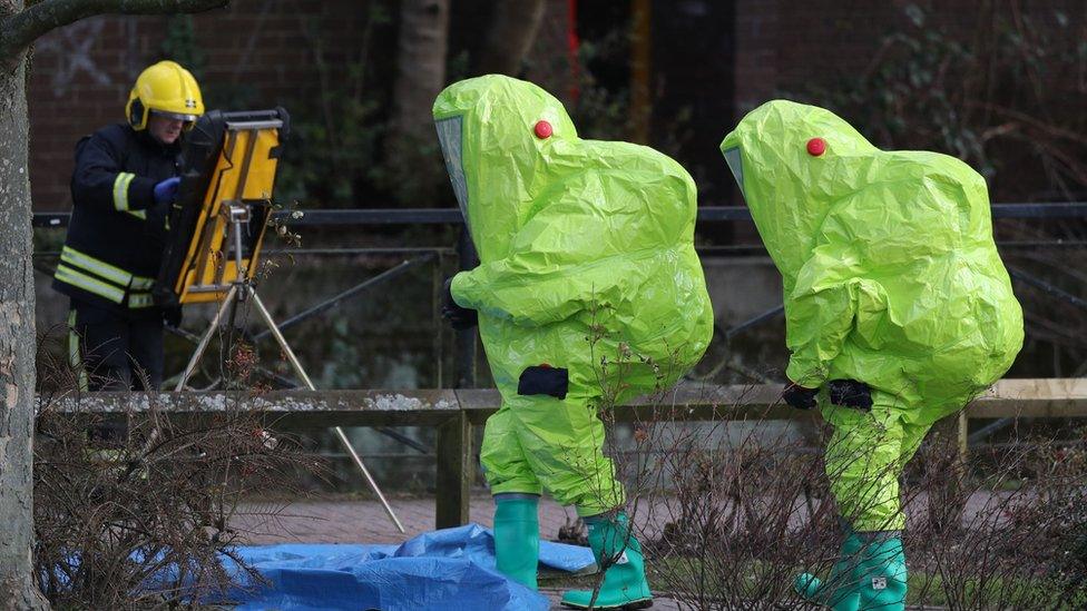 Investigators in hazmat suits walk near where Sergei and Yulia were found