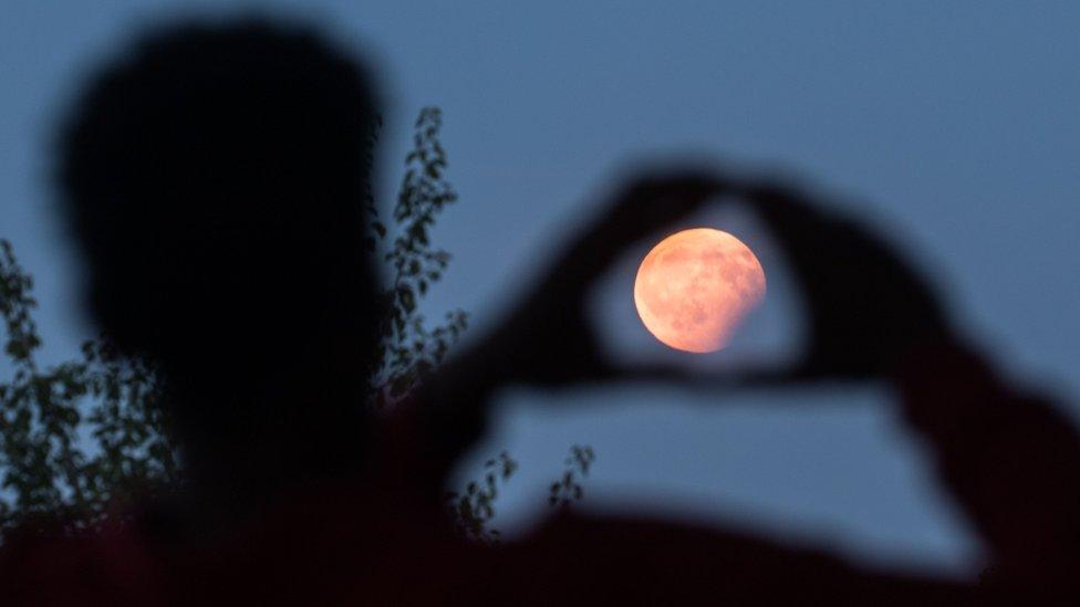 A man frames the moon with his hands during the lunar eclipse