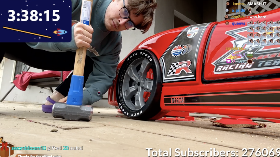 Ludwig poses next to a plastic red racecar bed frame with a sledgehammer.