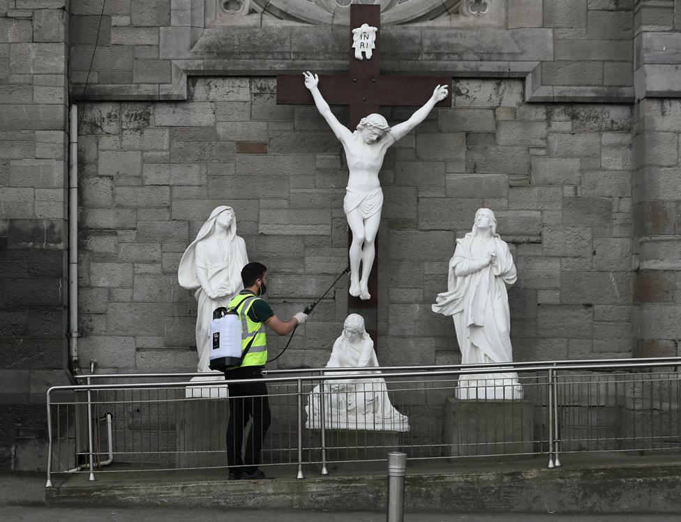 A man spraying disinfectant at a statue of the crucifixion of Jesus in Dublin on Good Friday