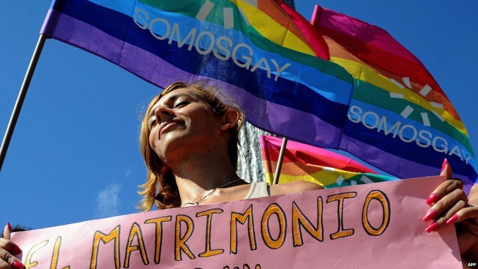 A gay marriage supporter holds a sign in front of a rainbow flag