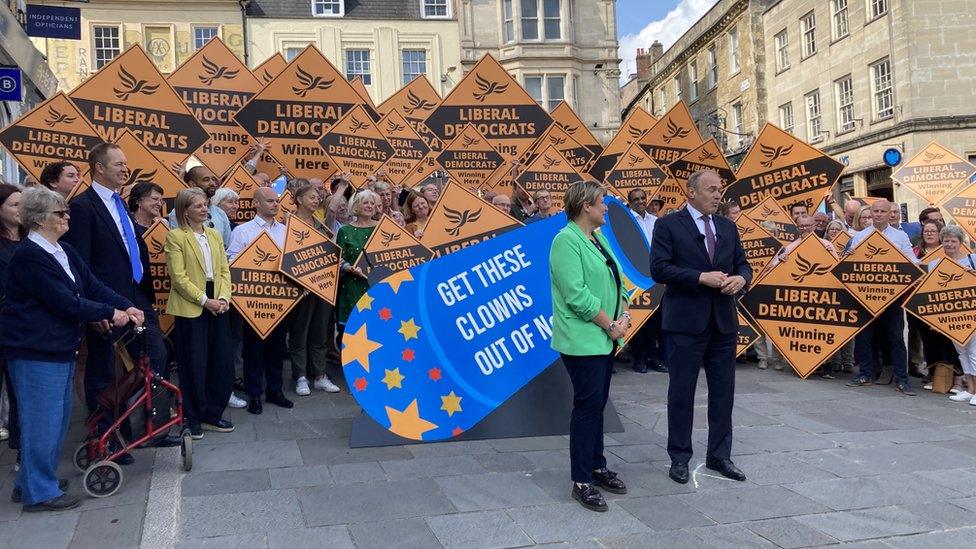 Sarah Dyke and Ed Davey standing in front of Lib Dem supporters