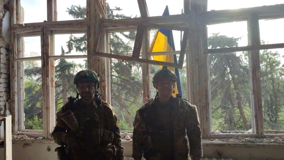 Ukrainian soldiers stand in front of a Ukrainian flag at a building, during an operation that claims to liberate the first village amid a counter-offensive, in a location given as Blahodatne, Donetsk Region, Ukraine, in this screengrab taken from a handout video released on 11 June 2023