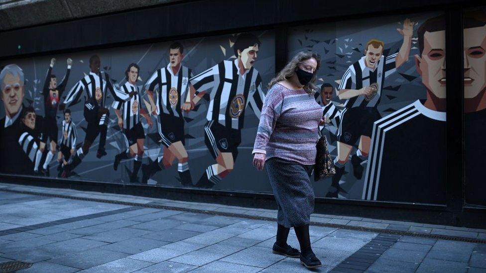 A woman wearing a mask walking past a Newcastle United mural in Newcastle