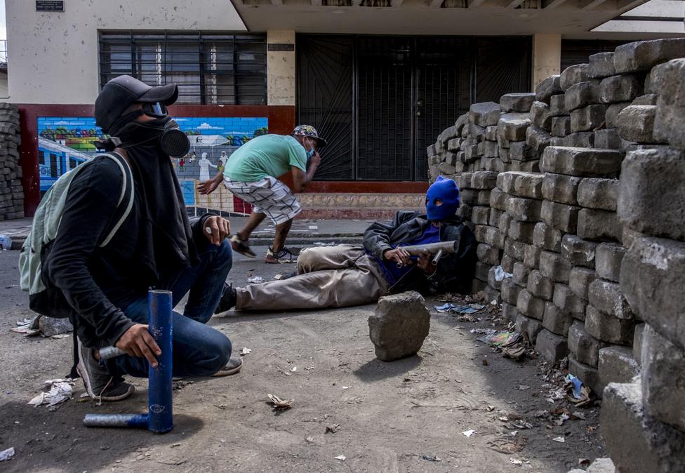 Masked youths with homemade mortars take cover behind a barricade as police bullets fly overhead