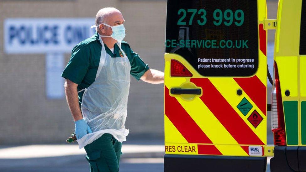 London Ambulance staff wearing PPE help a patient with an unknown condition from an ambulance at Queens Hospital