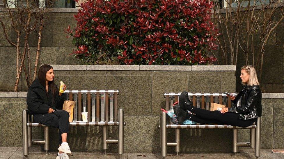 Two friends enjoy their lunch together at a safe distance in central Leeds on March 21, 2020, a day after the British government said it would help cover the wages of people hit by the coronavirus outbreak as it tightened restrictions to curb the spread of the disease.