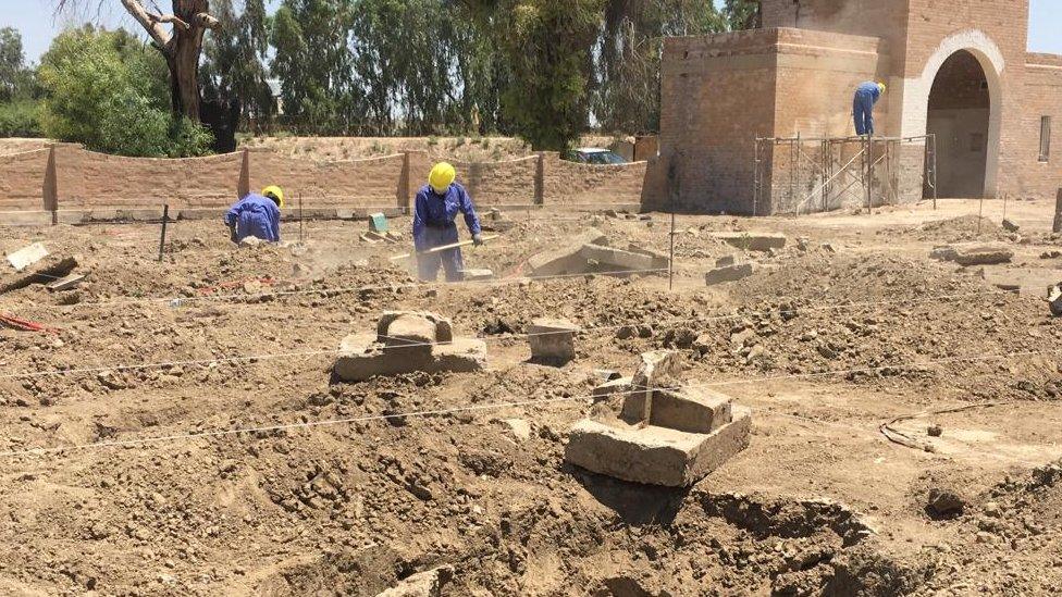 Workers in blue overalls and yellow hard hats are pictured using shovels