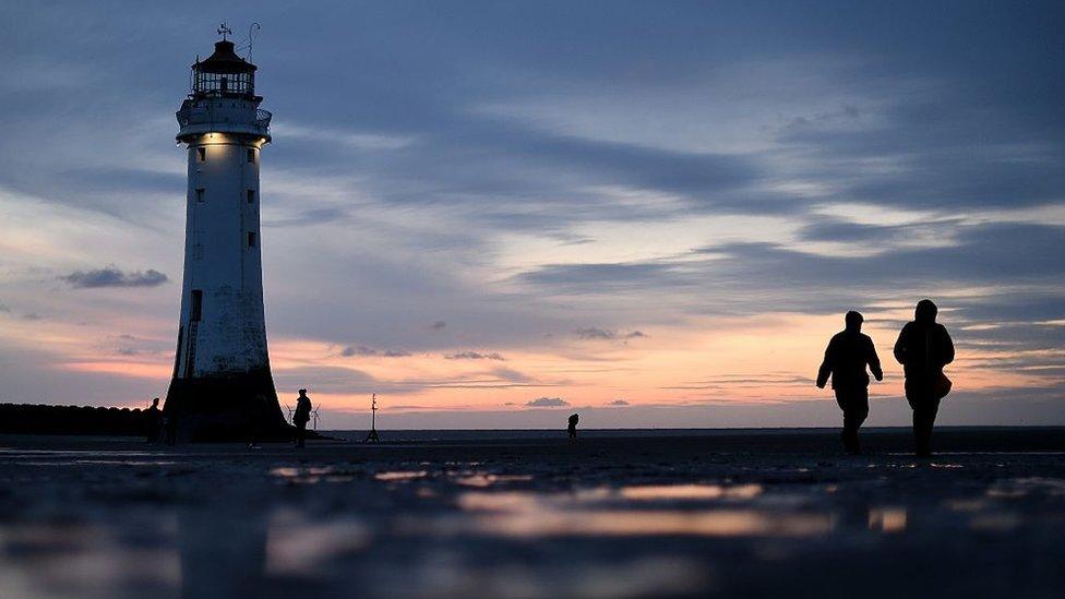 People walk along the beach at the mouth of the River Mersey at New Brighton, north-west England