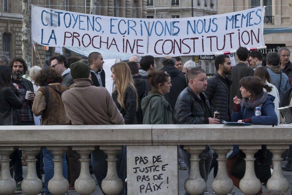 People gather next to a banner which reads "citizens, let's write ourselves the next constitution" on the Place de la Republique, in Paris