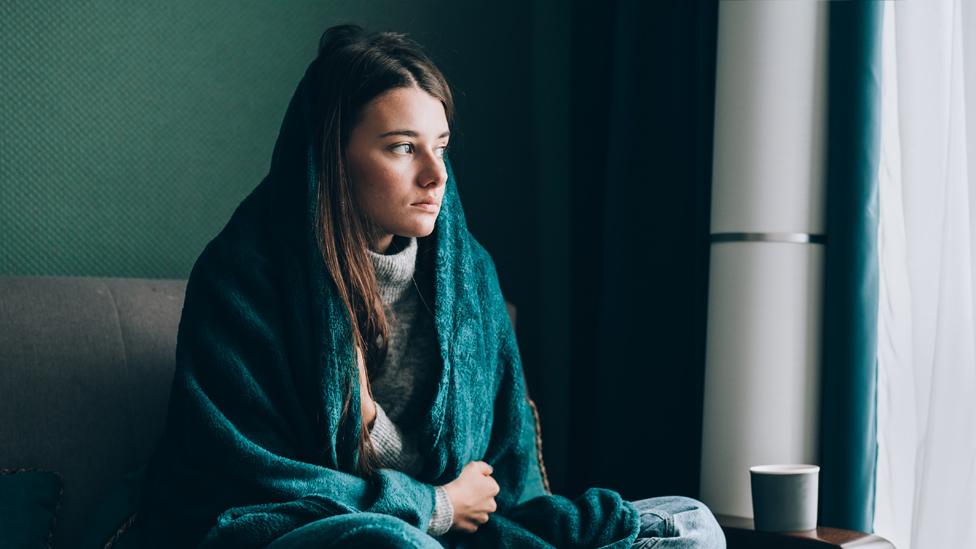 Young woman wrapped in a blanket in a cold house