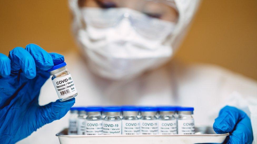 Healthcare professional in protective gloves & workwear holding & organising a tray of COVID-19 vaccine vials