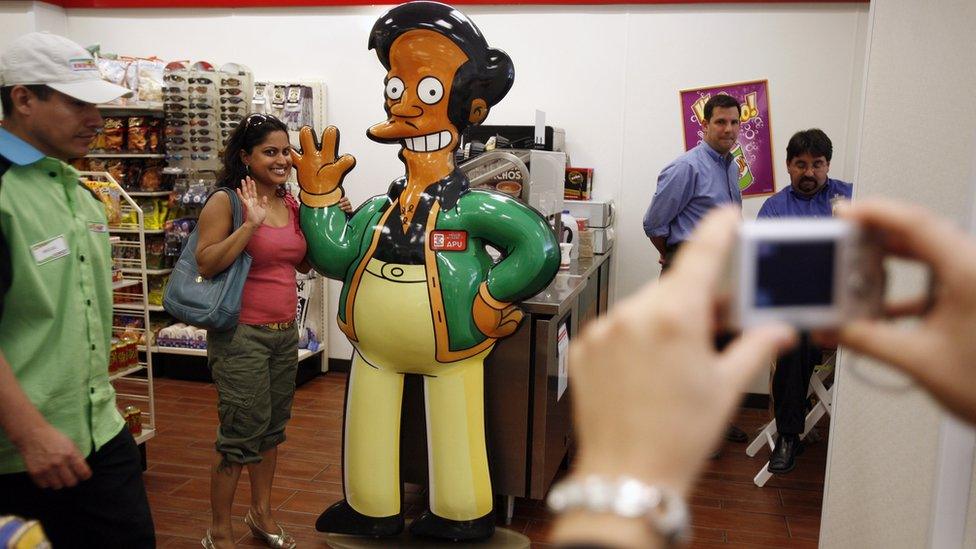 A person poses with a statue of Apu in a replica of the Kwik-E-Mart