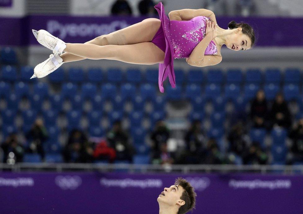 Ice skater Anna Duskova spins in the hair horizontally as her partner Martin Bidar looks up at her