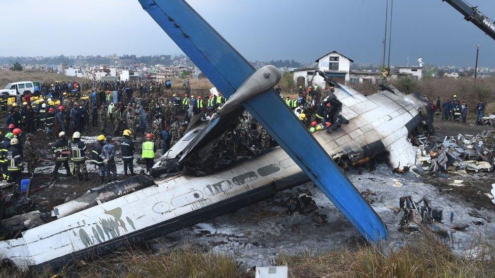 Nepali rescue workers gather around the debris of an airplane that crashed near the international airport in Kathmandu