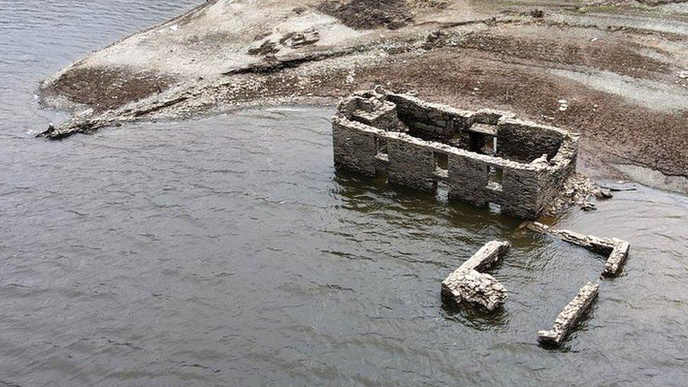 Stone farm buildings in water by the shore of a reservoir