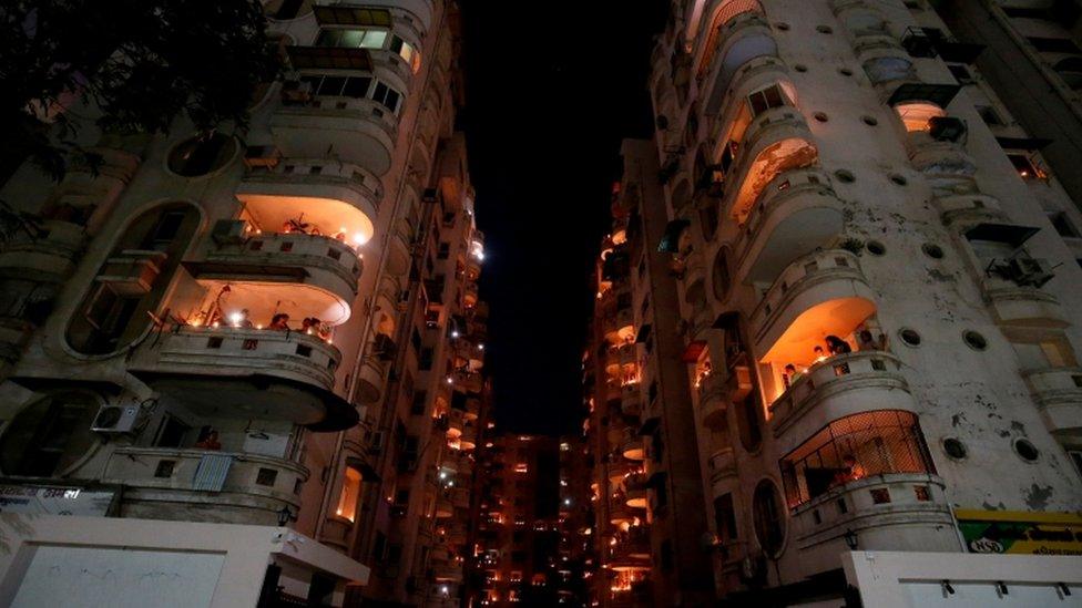 People stand on their balconies and light candles and oil lamps in India