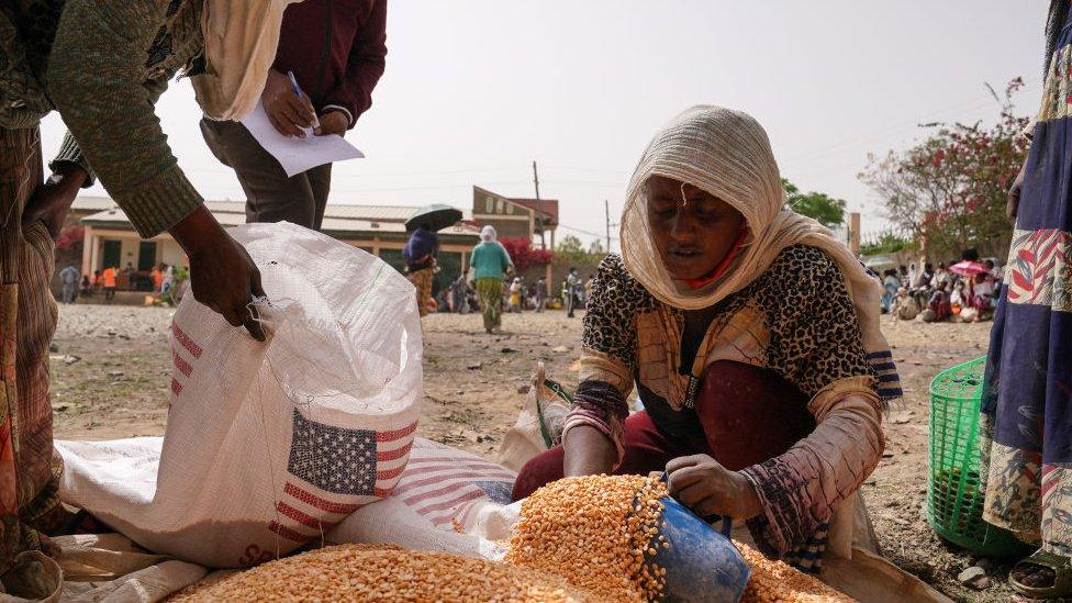 An aid worker distributes measured portions of yellow lentils to residents of Geha subcity