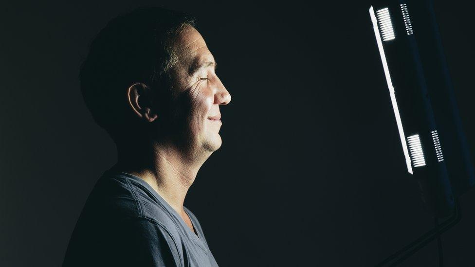 A man stands in front of a light box