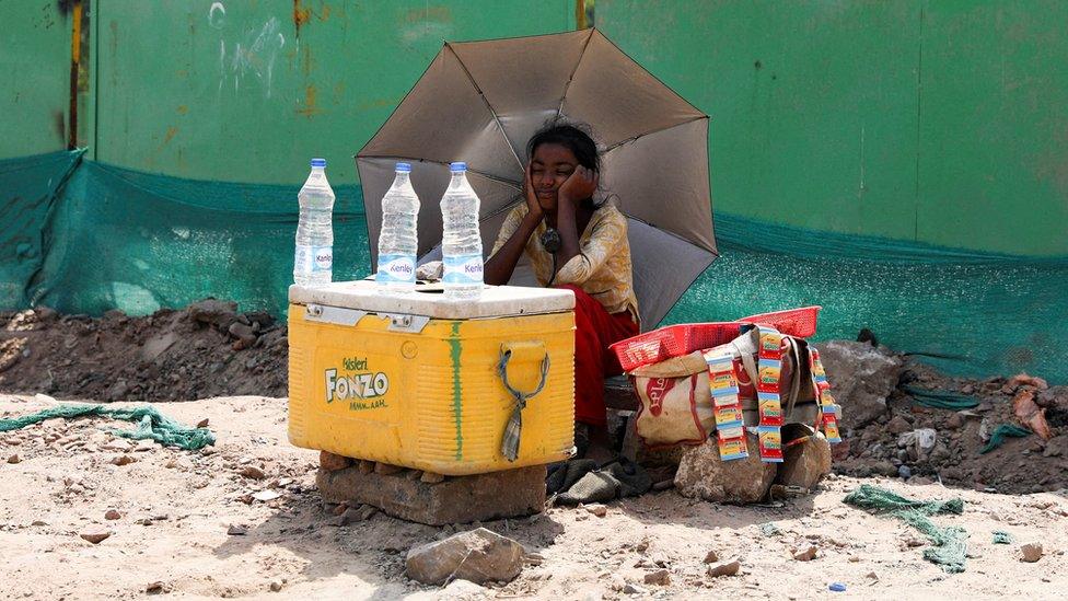 A girl selling water uses an umbrella to protect herself from the sun as she waits for customers on a hot summer day in Delhi on 27 April